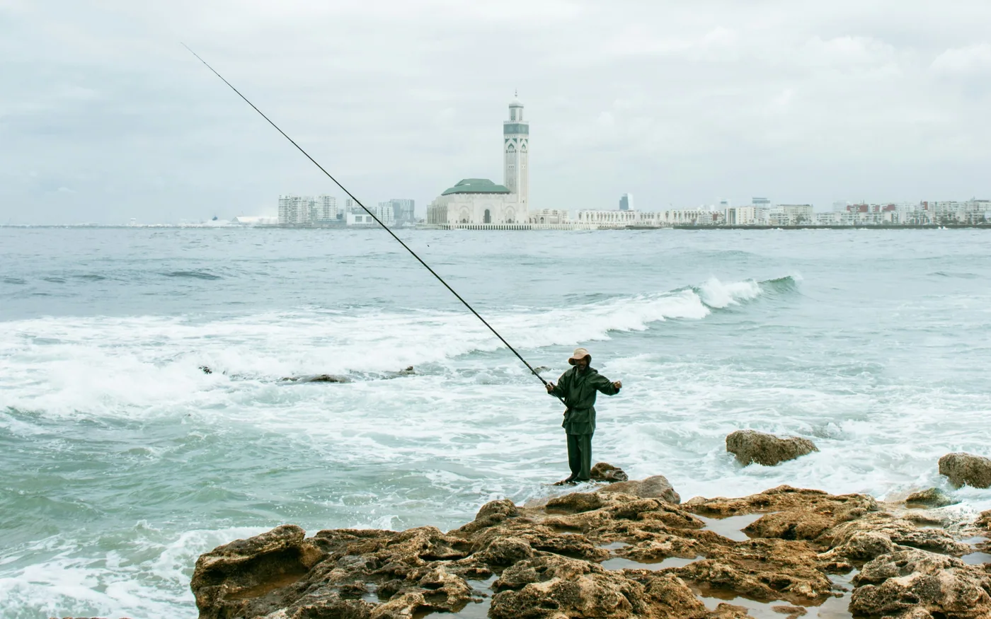 Fisherman on the rocks of the Casablanca shoreline, with the Hassan II Mosque on the horizon