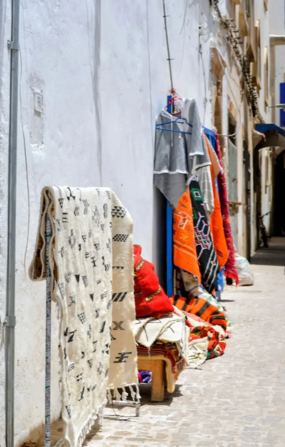 Tapis berbères et tissus colorés exposés dans une ruelle blanche de la médina d'Essaouira