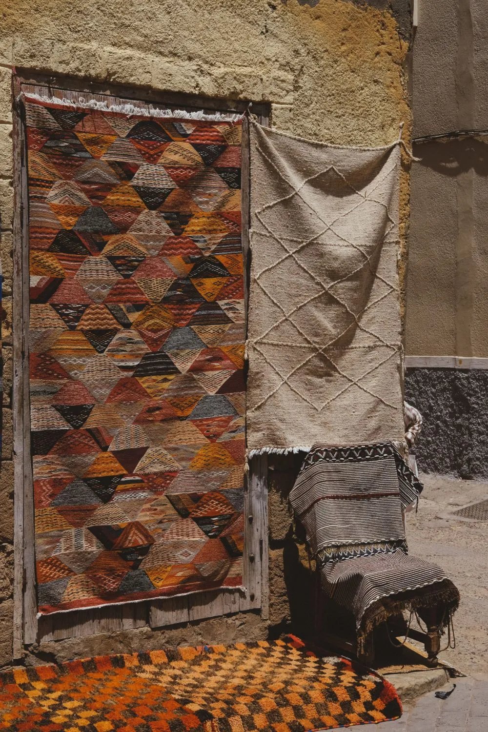 Amazigh rugs with geometric patterns hanging against an earthen wall