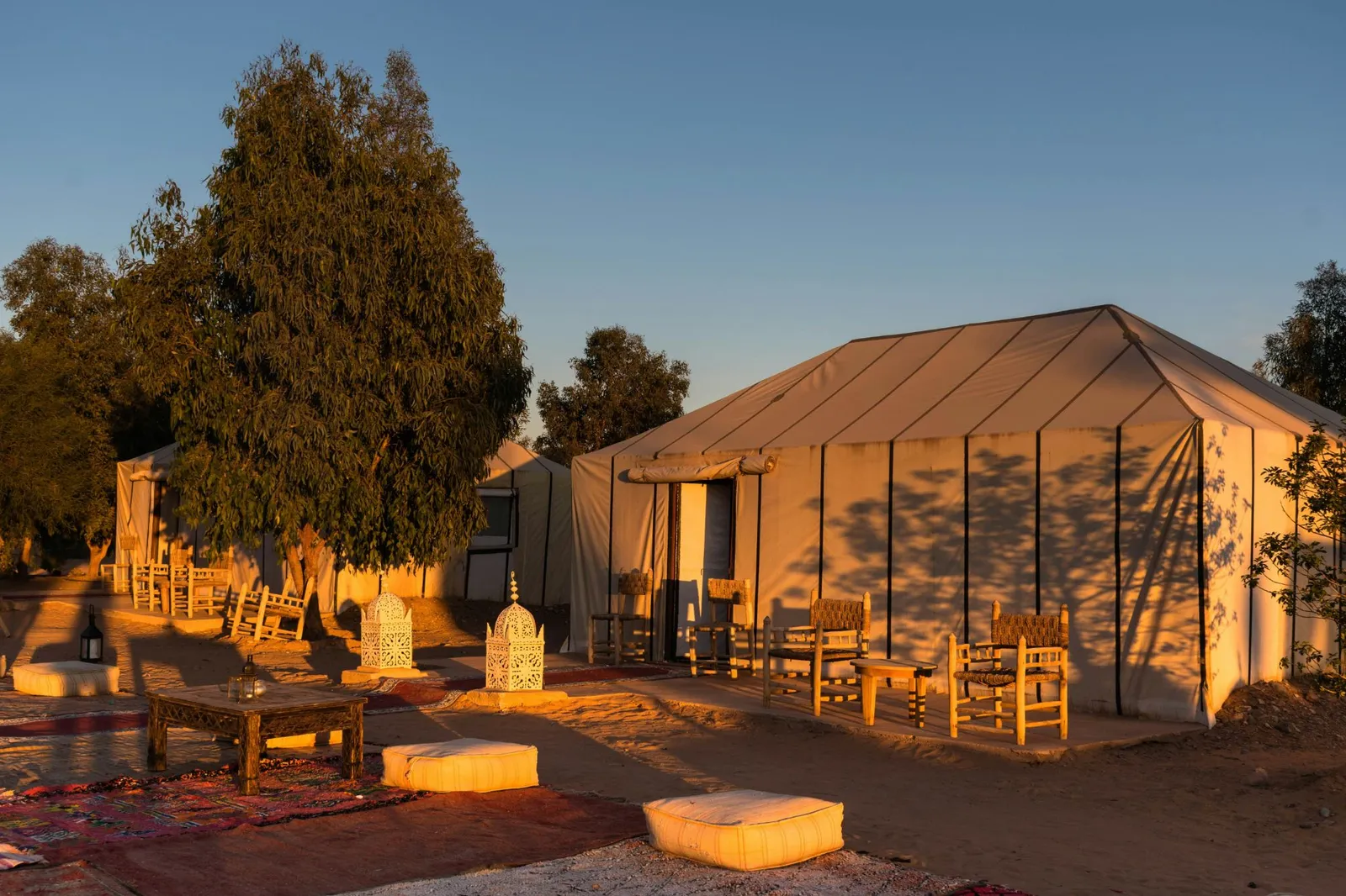 Camp de tentes traditionnelles au coucher du soleil, avec lanternes et coussins