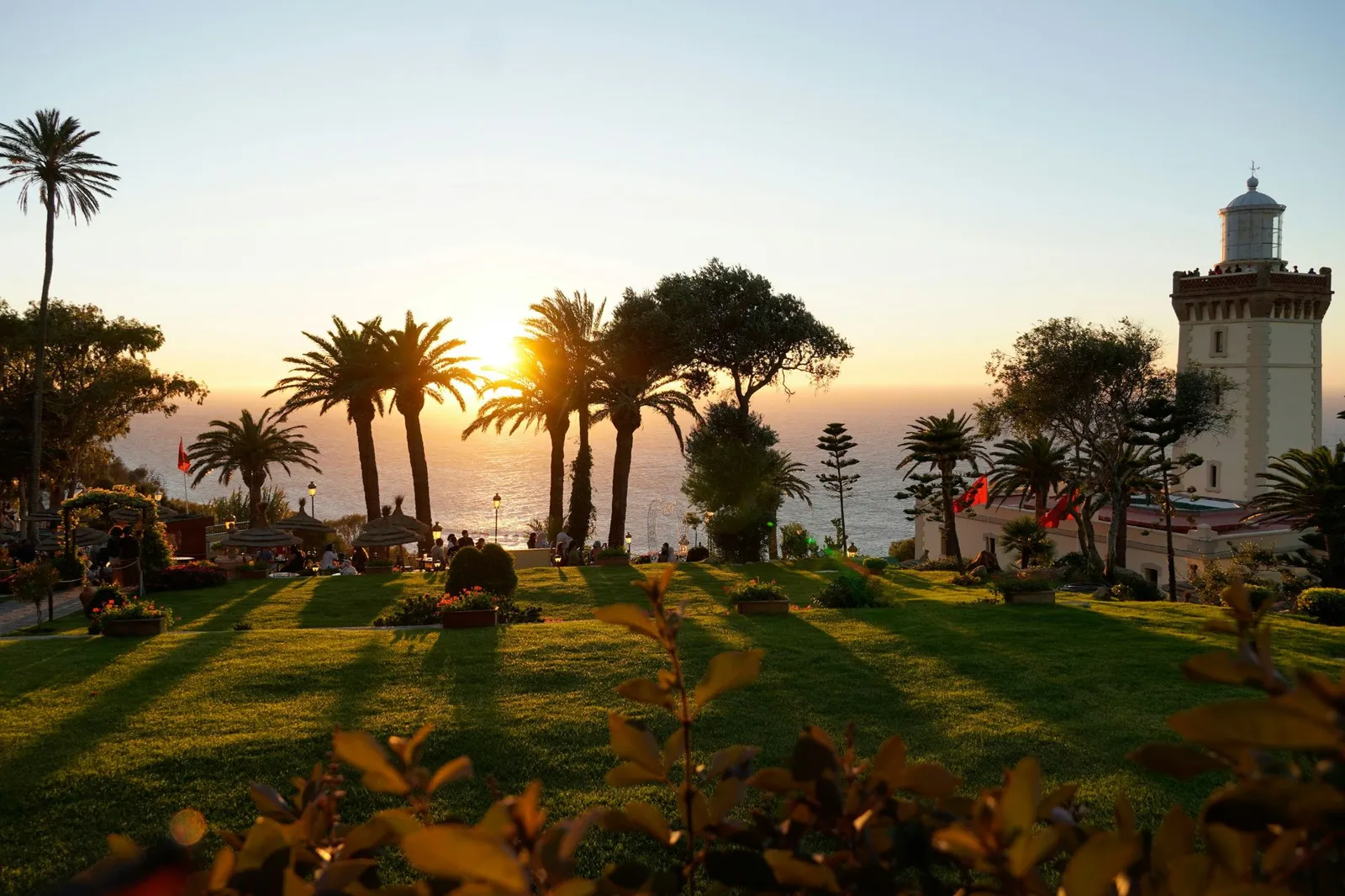Jardín al atardecer con palmeras y el faro del Cabo Espartel