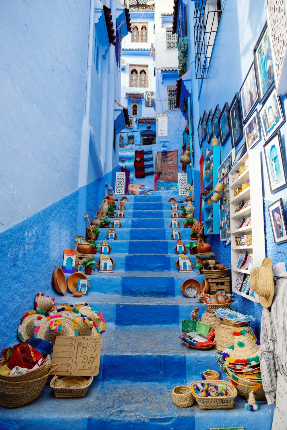 Scalinata blu di Chefchaouen decorata con ceramiche, cappelli di paglia e quadri