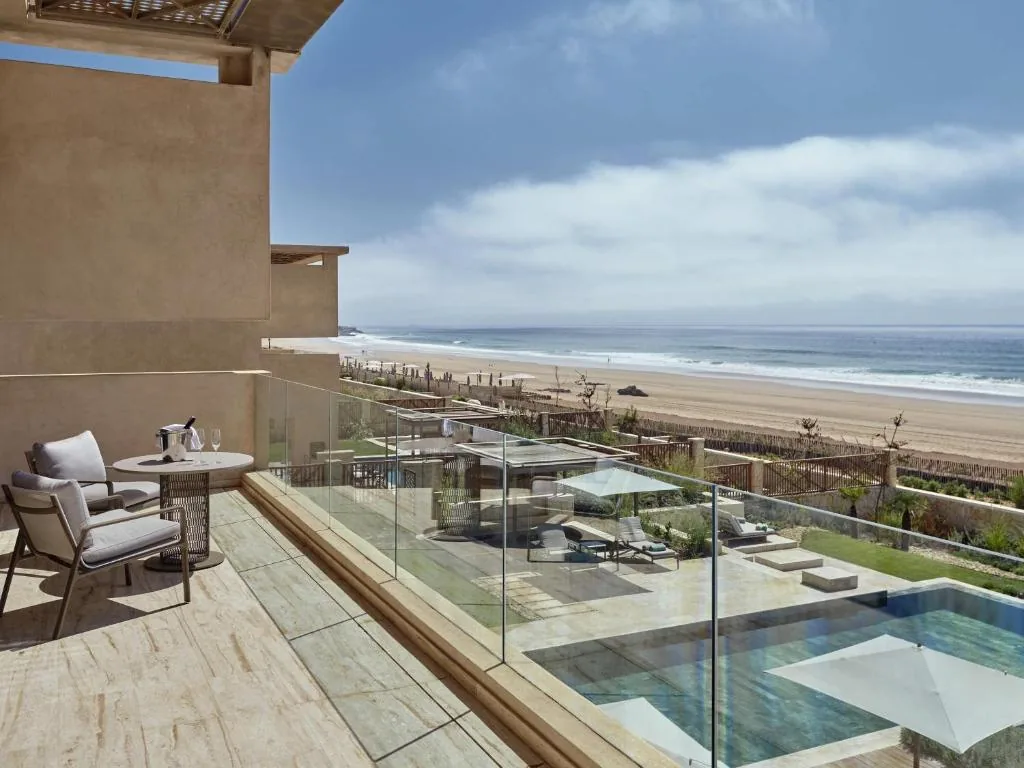 Balcón con barandilla de cristal con vistas a la playa y una piscina en la parte inferior