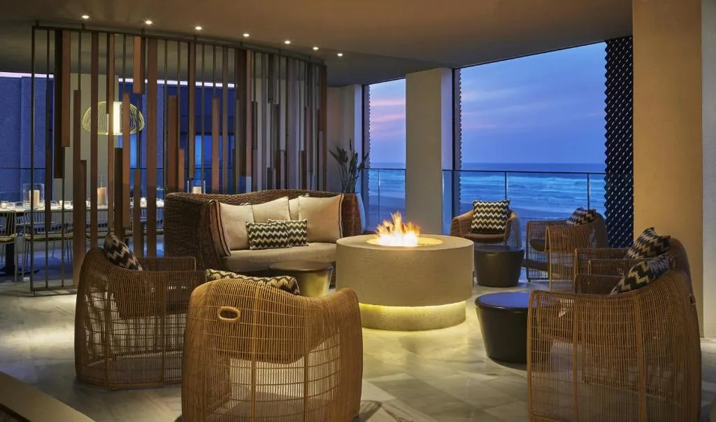 Salon en terrasse avec fauteuils en rotin tressé autour d'un foyer rond, face à l'océan