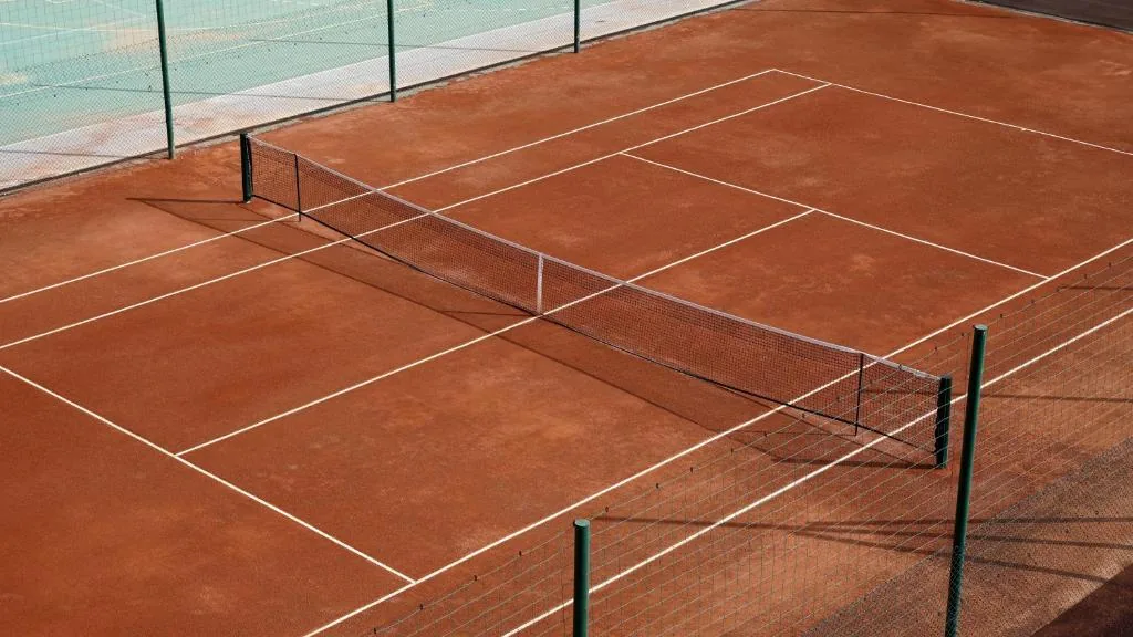 Red clay tennis court edged by a fence
