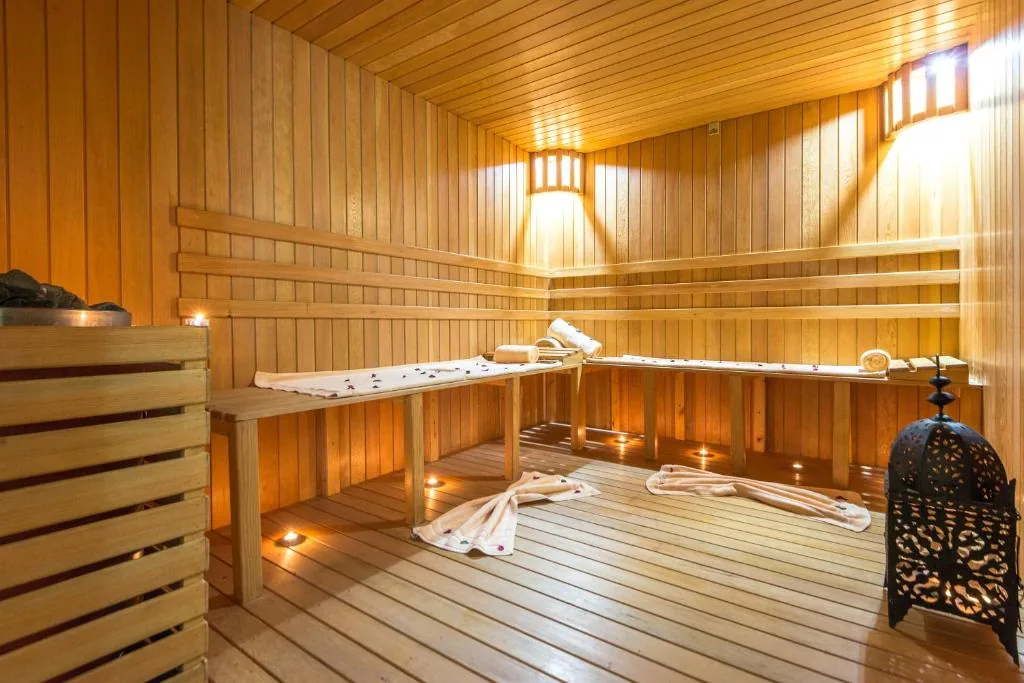 Sauna aus hellem Holz mit Bänken, gedämpftem Licht und durchbrochener Metalllaterne