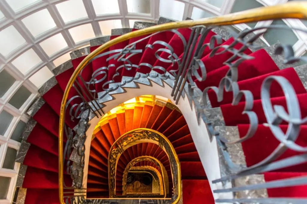 Wendeltreppe von oben, mit einem roten Teppich und einem vergoldeten Handlauf