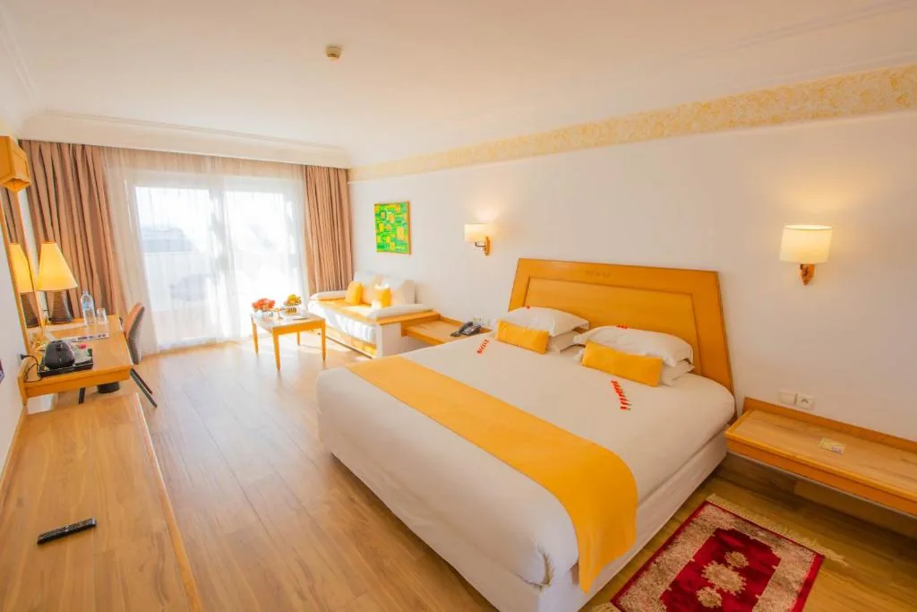 Bright room with a large bed, a yellow bed runner, a lounge corner and large windows