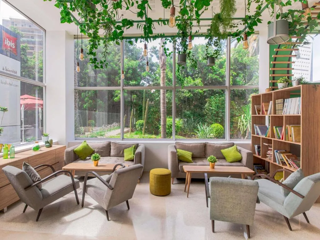 Salón luminoso con una estantería, sillones y grandes ventanales con vistas a la vegetación