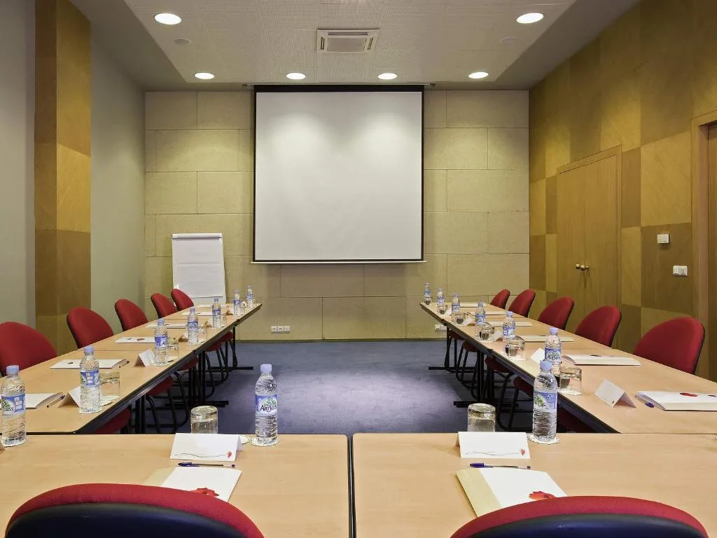 Sala de reuniones con mesas en U, sillas rojas y una pantalla de proyección