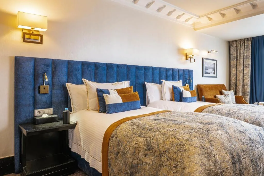Zimmer mit einem blau gepolsterten Kopfteil, einer gemusterten Tagesdecke und Nachttischlampen