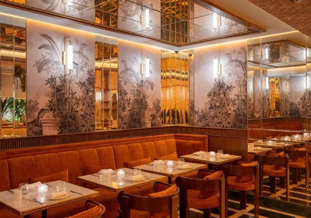 Sala de restaurante con banquetas naranjas, mesas de mármol y un decorado de follaje en las paredes
