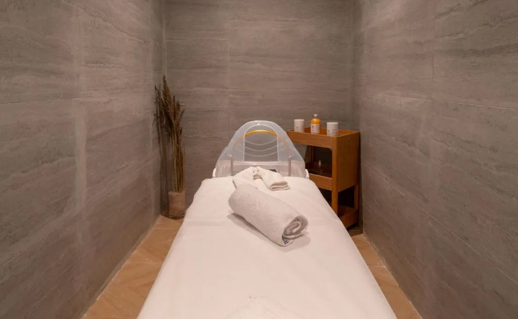 Treatment room with grey stone walls, with a massage table covered in white towels
