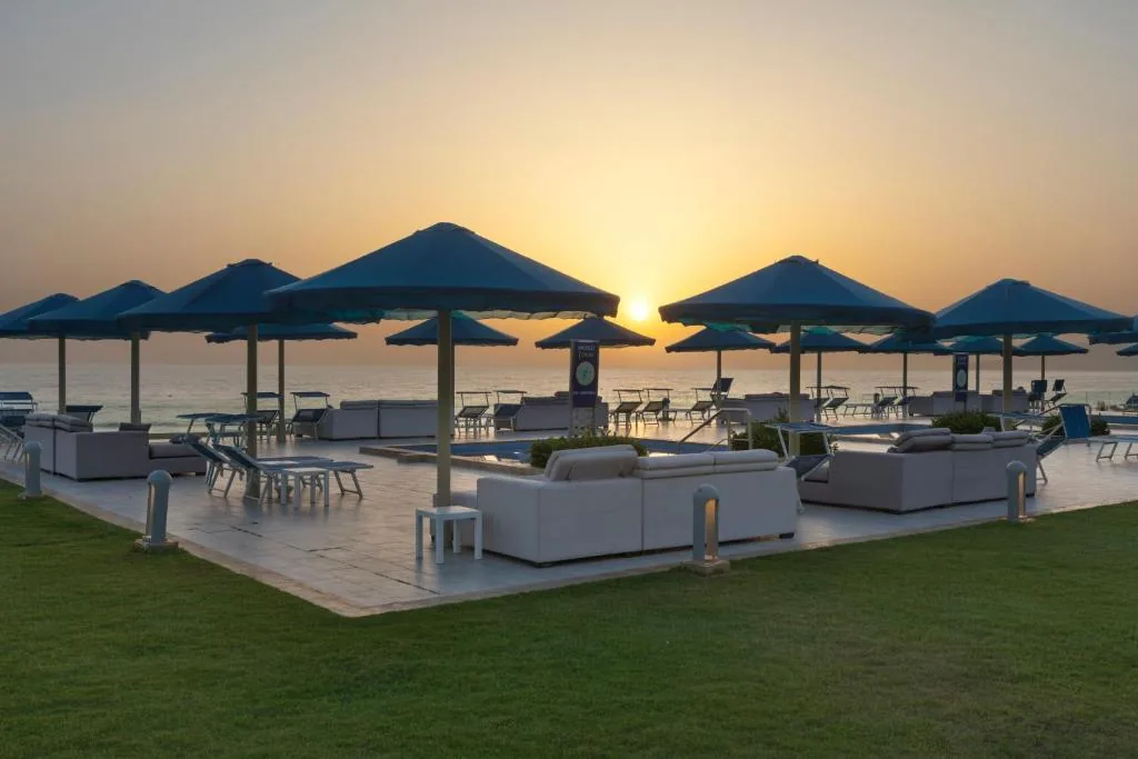 Seaside terrace at sunset, with dark-blue parasols, sofas and a lawn