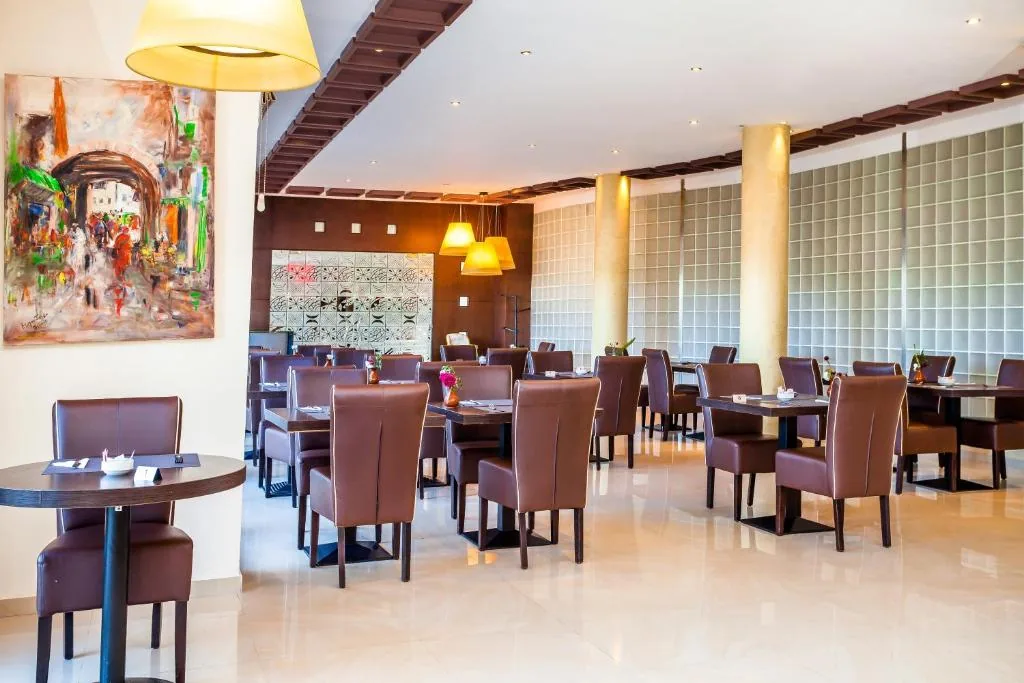 Large, bright dining room with wooden tables, brown chairs and a colourful painting on the wall