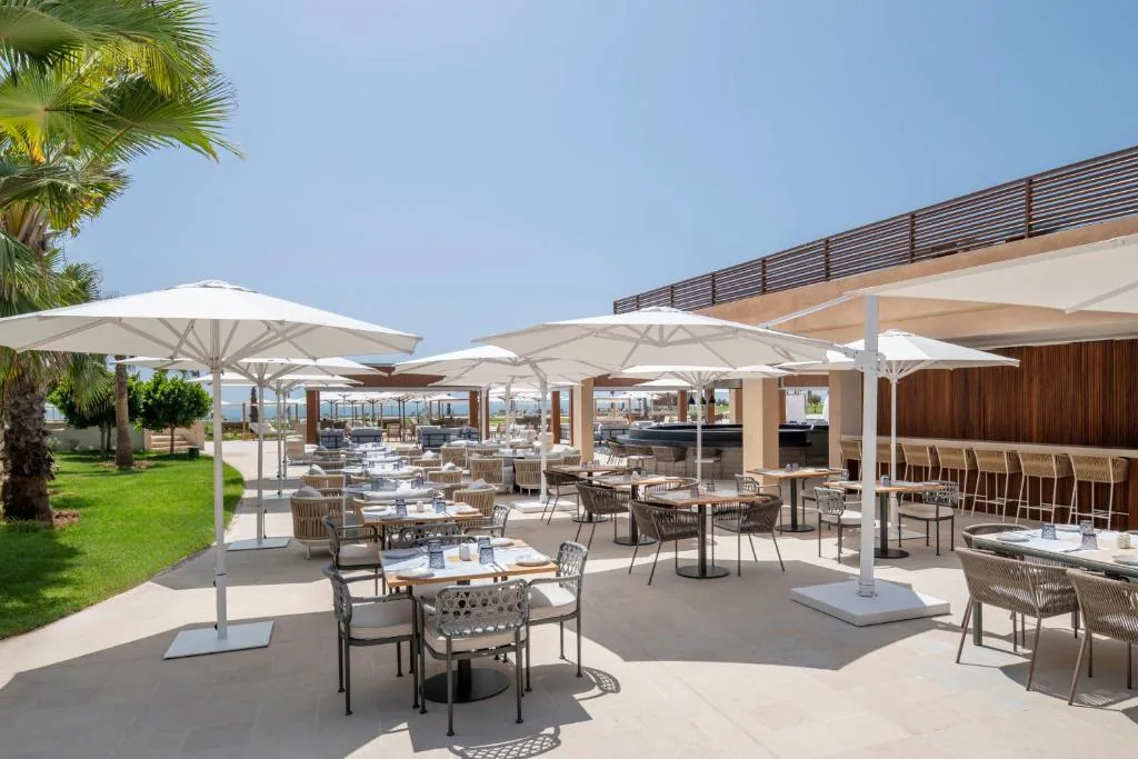 Restaurant terrace with large white parasols, tables and a lawn, facing the sea