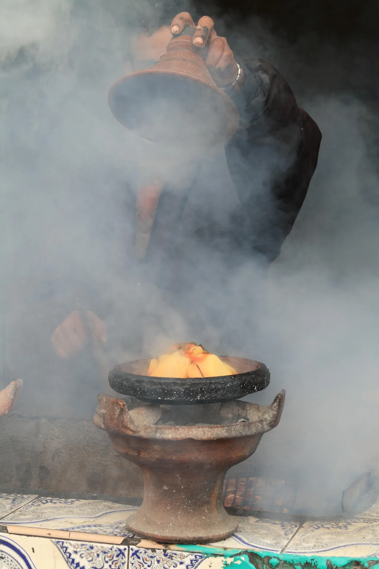 A clay tagine cooking over glowing embers in the smoke