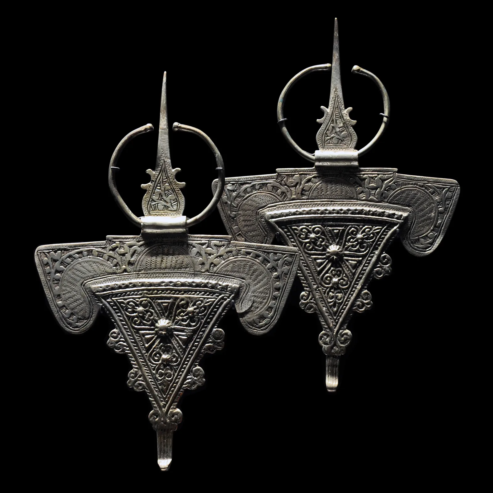 Two finely engraved Amazigh silver fibulae against a black background.