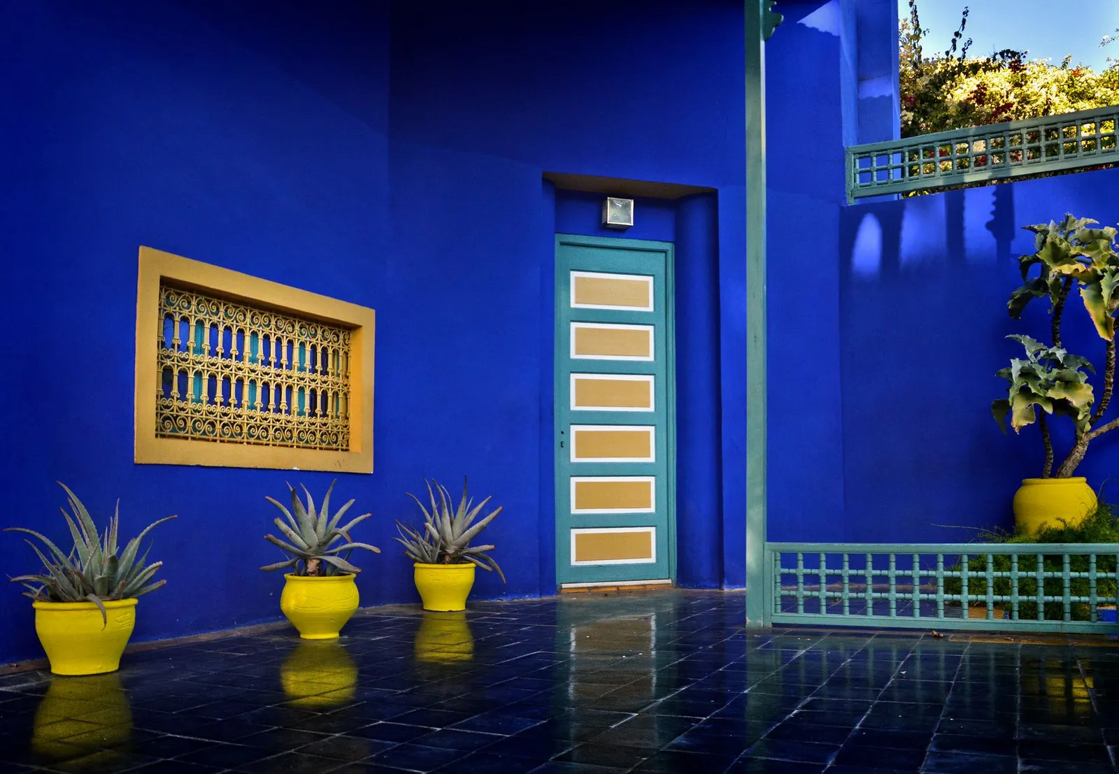 Cour aux murs bleu Majorelle, fenêtre ajourée et jardinières jaunes au Jardin Majorelle